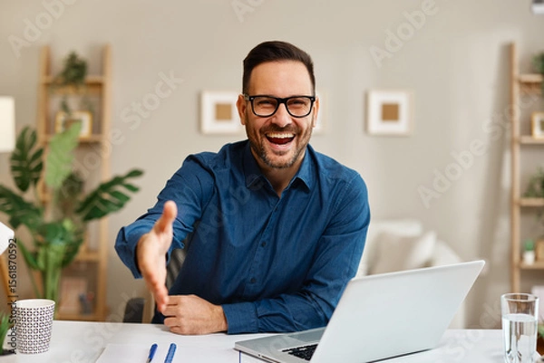 Obraz Smiling businessman offering handshake during video conference at home office