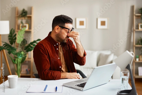 Obraz Tired businessman rubbing eyes while working from home office
