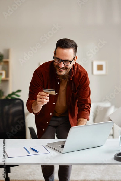 Obraz Smiling freelancer making online payment using credit card at home office