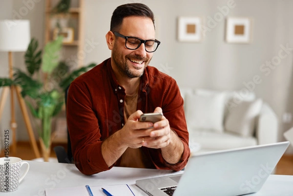 Obraz Happy entrepreneur using smartphone and laptop at home office