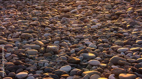 Fototapeta Sunlit pebble beach. Smooth stones are illuminated by warm sunlight. Beautiful interplay of colors and textures. Theme related to zen and relaxation.