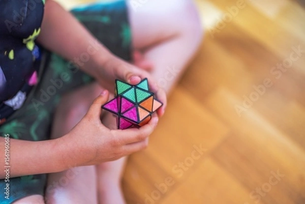 Fototapeta Child sitting on floor holding colorful star-shaped puzzle cube with both hands. Sweden.