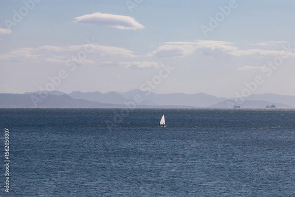 Obraz Alone white sailboat in the middle of the blue sea against the silhouette of mountains