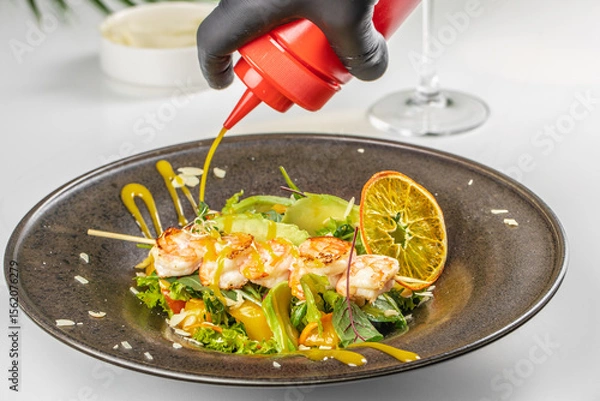 Obraz A close-up of a shrimp and vegetable salad being drizzled with bright yellow dressing, garnished with citrus and fresh greens