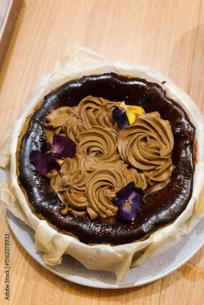 Fototapeta vertical photo of close up of freshly homebaked basque cheesecake with earl grey tea cream as topping and flower as decoration wrapped by a paper