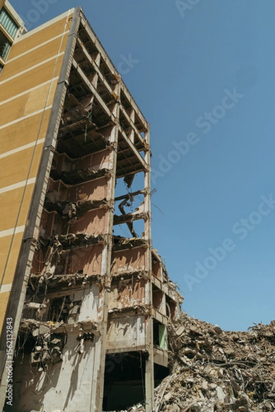 Obraz Ruins of a collapsed residential building, surrounded by rubble and broken concrete. Partially destroyed high-rise building after accident, earthquake or war