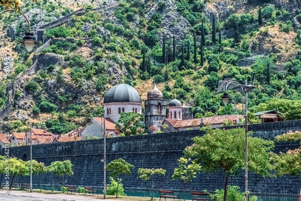 Fototapeta Ancient stone walls and dome of the Serbian Orthodox Church of St. Nicholas in Kotor, Montenegro, set on a backdrop of rugged mountains. Scene showcases the rich history and scenic beauty of Kotor