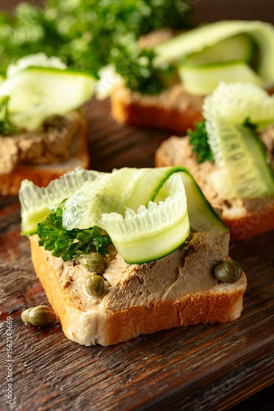 Obraz  Open sandwiches with pate, cucumber, capers, and parsley on a old cutting board.