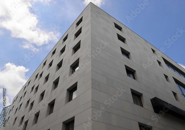 Obraz many rows of glass windows frames  on large square grey concrete tiles wall of business office building. angle view. gray tiled exterior. Subotica Serbia City centre Blue cloudy sky heaven