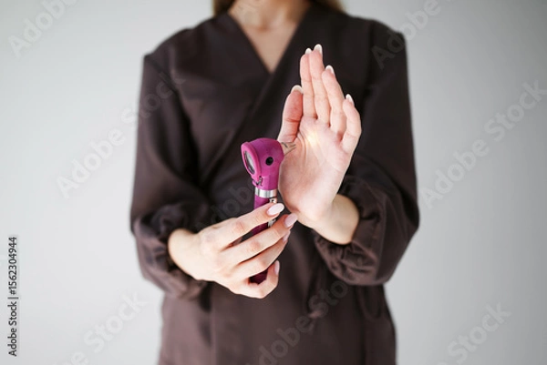 Fototapeta Close-up of woman's hands testing a pink otoscope by shining light onto her palm. Concept of medical diagnostics, ENT tools and health check. 