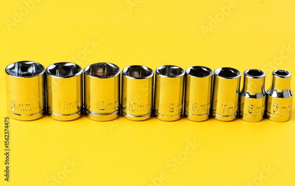 Fototapeta Set of chrome socket wrench heads arranged in row on yellow background close up