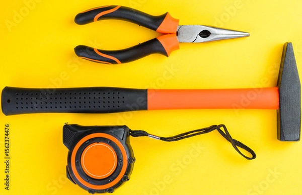 Fototapeta Top view of hammer measuring tape and pliers on yellow background construction tools
