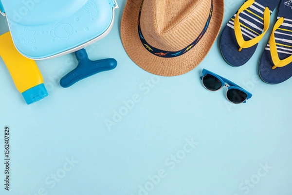 Obraz Kids beach summer frame from suitcase, sun protection cream, straw hat, sandals and sunglasses on blue background. Top view. Copy space