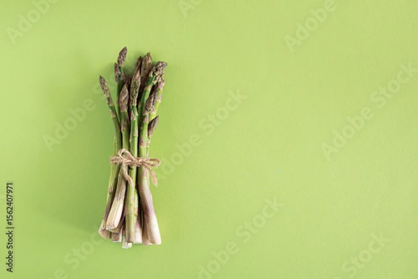Obraz Fresh asparagus tied bundle on vibrant green background. Top view