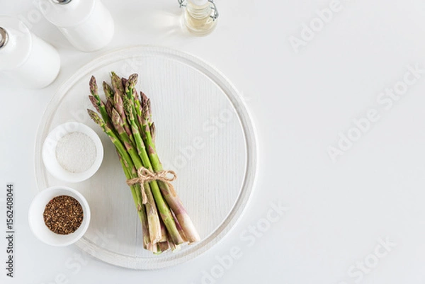 Obraz Fresh asparagus shoots with spices on white table. Top view
