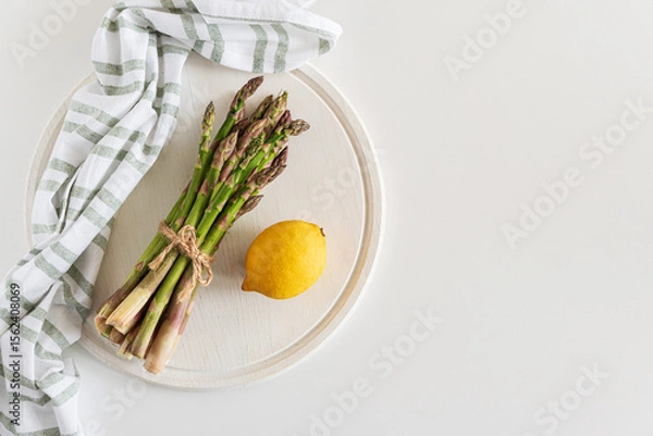 Obraz Fresh asparagus shoots with lemon on white table. Top view