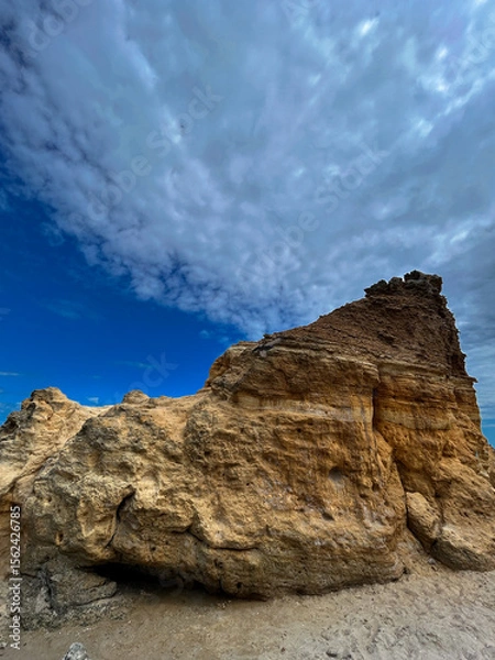 Fototapeta Dramatic yellow rock formation on a beach in Odesa, Ukraine, under a dynamic cloudy sky. The textured sandstone contrasts with the deep blue horizon, creating a powerful natural landscape. A scenic