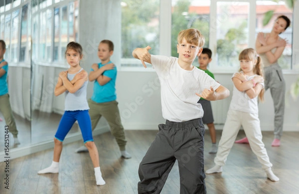 Fototapeta Boy with friends repeat teaches sequences of movements during training, train to perform electro dance, enjoys active hobby to her favorite music. Unrecognizable female teacher administer conduct