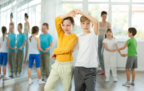 Fototapeta Positive preteen children learning to dance waltz in pairs in choreography class