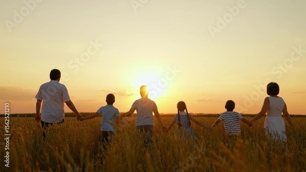 Obraz Parents children go holding hands walk through wheat field. Happy family of farmers walk in nature, sunset. Teamwork group of people travel walk wheat field. Group of people in nature sunny day, kids