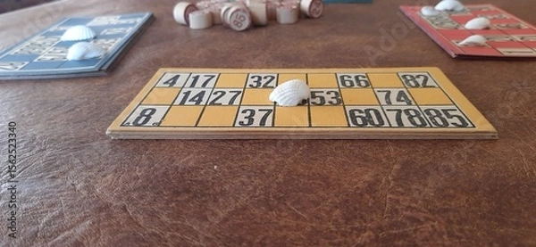 Fototapeta Close-up of a yellow lottery card with a white seashell marking a number, highlighting the originality of the markers