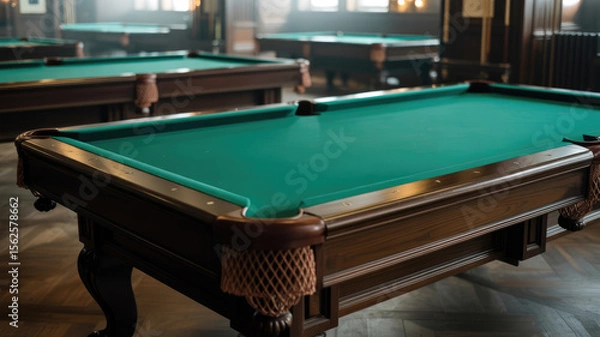 Fototapeta A green pool table sits in a room with other pool tables. The room is dimly lit, giving it a cozy atmosphere