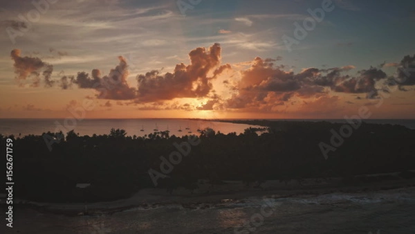 Obraz The setting sun warm glow over Rangiroa island in French Polynesia, illuminating sailboats anchored near shore creating a breathtaking aerial view of paradise. Remote wild nature, exotic summer travel