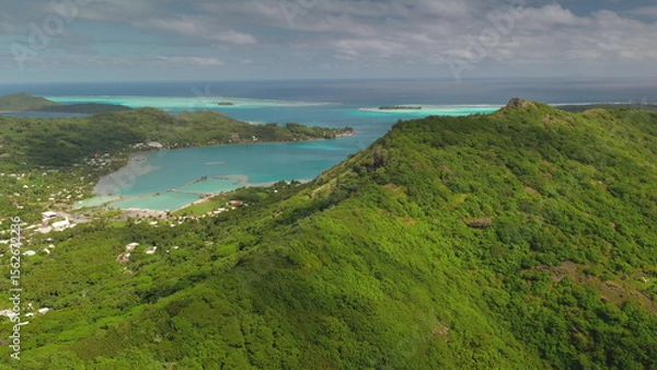 Fototapeta Tropical vegetation covers the mountain slopes of Bora Bora, a volcanic island in French Polynesia, while turquoise waters lap against the sandy shores of the lagoon