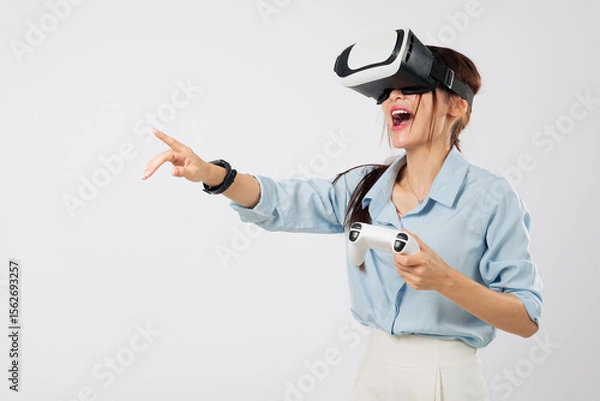 Fototapeta VR game excitement with Young Asian woman pointing during VR game play, immersed in joyful virtual reality experience. isolated studio white background