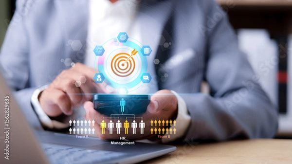 Fototapeta Businessman using mobile phone with virtual HR management interface. Human resource recruitment, digital teamwork, and target planning concept.
