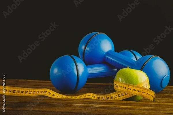 Fototapeta Blue dumbbells with green apple and measuring tape