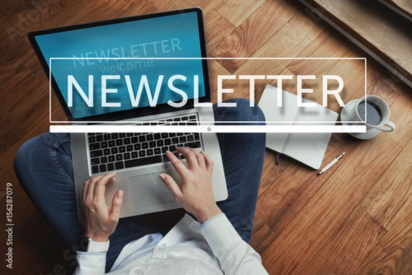 Obraz Top view of young woman sitting on the wooden floor with laptop and coffee with newsletter inscription in the foreground