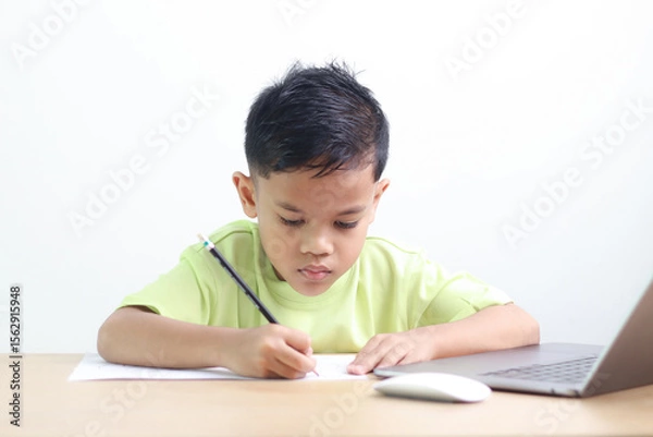 Fototapeta Young boy studying and doing homework at home with notebook and laptop. Concept of distance learning, education, homeschooling, and online classes for children.