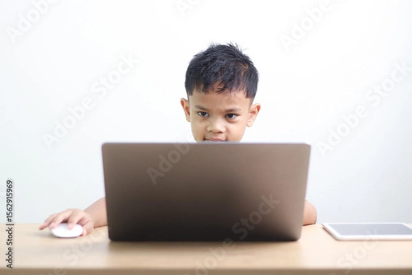 Fototapeta Young boy studying and doing homework at home with notebook and laptop. Concept of distance learning, education, homeschooling, and online classes for children.