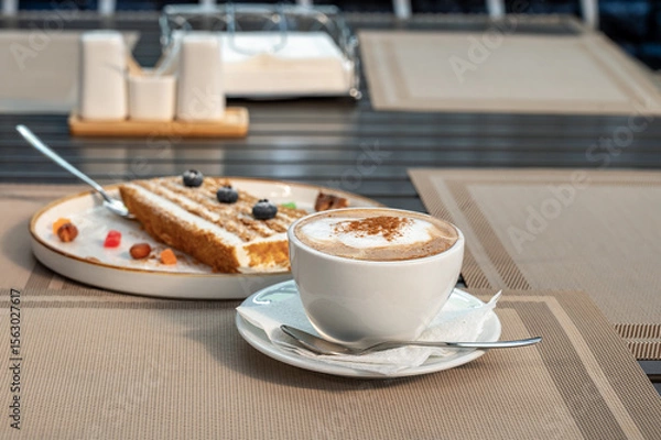 Fototapeta Cup of coffee, a piece of honey cake on a table in a sidewalk cafe.