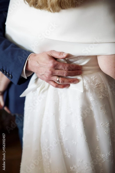 Obraz Close up of a grooms hand hugging the bride in white dress, back view