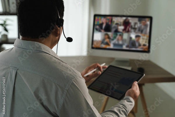 Obraz Virtual Meeting and virtual conference person participating virtual meeting using headset, tablet, and computer monitor displaying multiple people