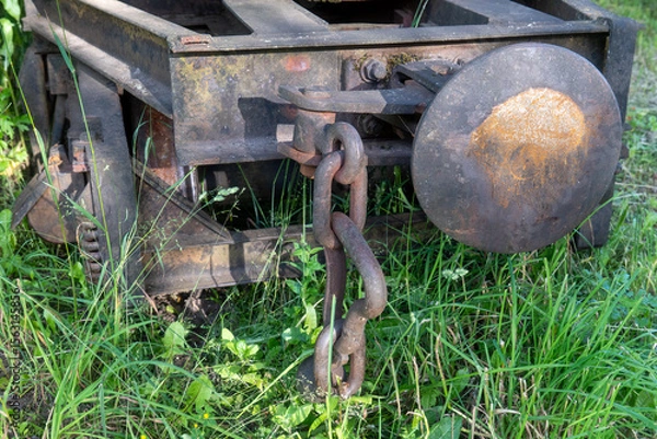 Fototapeta Close-up of rusty coupling chain and buffer on abandoned narrow gauge railway wagon overgrown with grass in summer forest, symbol of decay and forgotten transportation