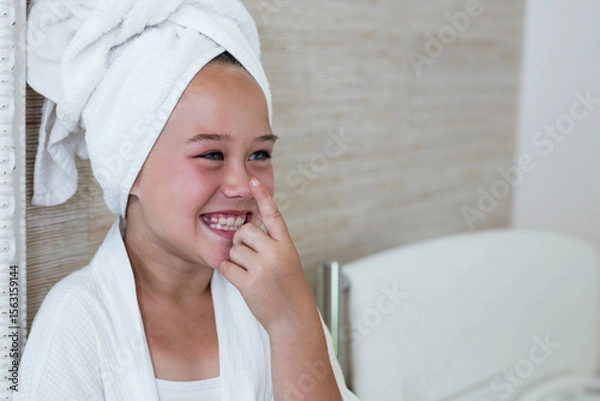 Fototapeta White bathrobe and towel turban resting on bench while beige tile walls gleaming in home bathroom