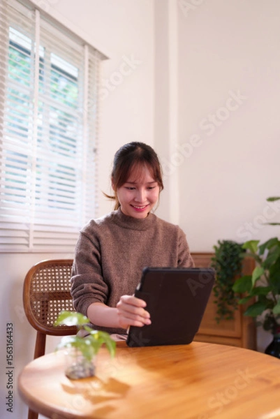 Fototapeta Asian Young Adult Woman Engaged with Tablet Device at Home Daily Lifestyle Digital Connectivity AI Integration Smart Living Modern Technology Use