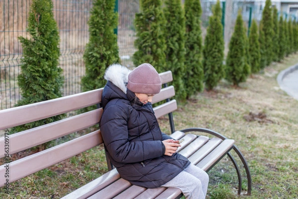 Fototapeta Kid using phone alone on park bench