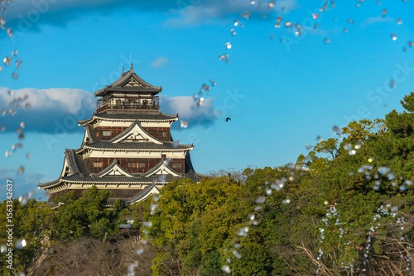 Fototapeta Airborne water droplets from a fountain create sparkling, dynamic frame for the historic Hiroshima Castle. Unique perspective captures iconic Japanese landmark in Hiroshima, Japan, on a beautiful day