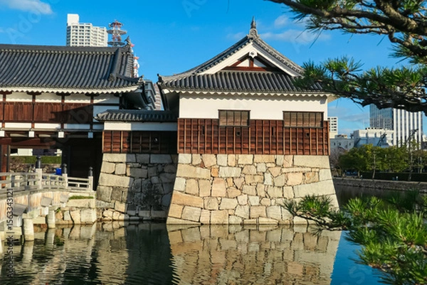 Fototapeta Turret of historic Hiroshima Castle stands on its massive stone foundation, perfectly reflected in tranquil moat. Peaceful scene in Hiroshima, Japan, contrasts ancient architecture with modern city