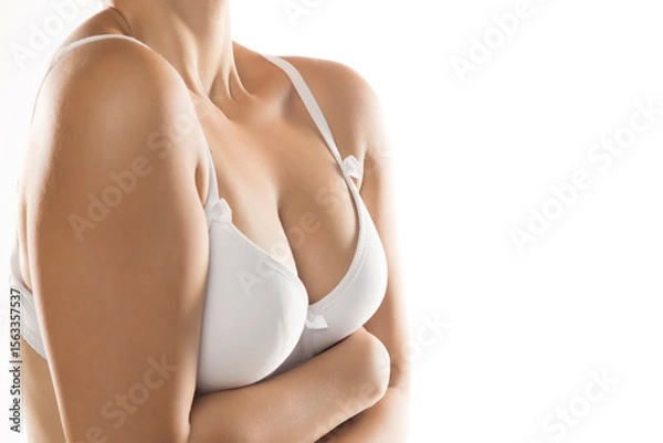 Fototapeta Close-up of woman's chest and crossed arms in white bra, smooth skin, studio shot on white background