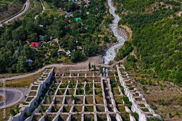Fototapeta A protective dam in the Talgar gorge. A mountainous area with different vegetation and a river.