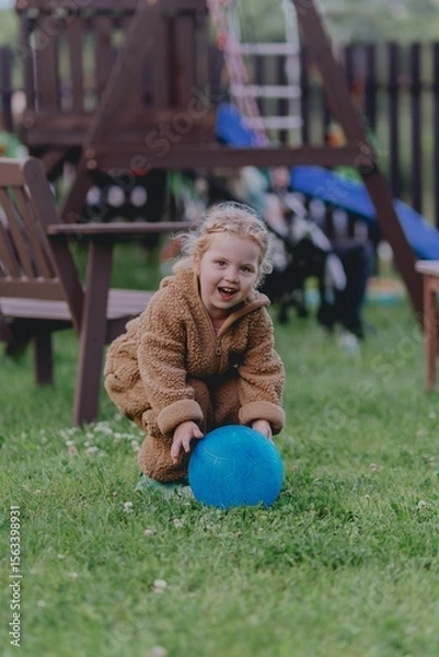 Fototapeta Beautiful 3-year-old girl playing on a neighborhood playground swinging, running on the grass, and enjoying fresh air. A joyful, natural moment full of real emotions and unaltered beauty