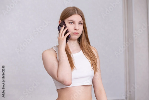 Obraz Young woman stands while talking on a smartphone in a bright indoor space during a casual day