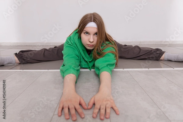 Obraz Young girl practices flexibility and stretching on the floor in a minimalist indoor space during morning training session