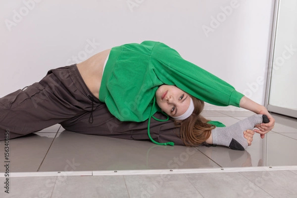 Obraz Yoga enthusiast performs a deep stretch while wearing a green hoodie in a modern gym setting during the morning