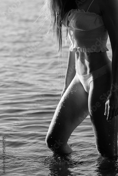 Fototapeta woman wades through the shallow water of a lake, her figure illuminated by sunlight. Water droplets cling to her skin, creating a tranquil and serene atmosphere perfect for relaxation